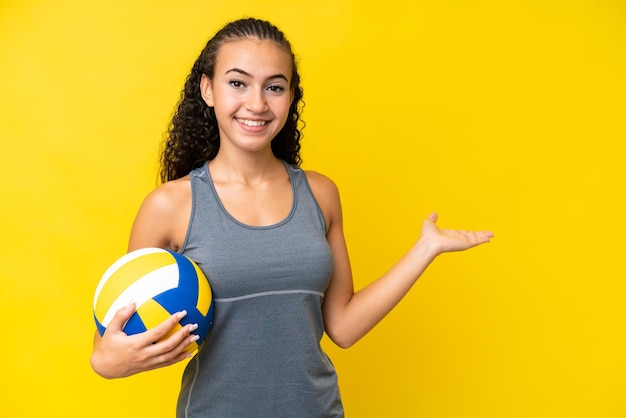 Jovem jogando vôlei isolada em fundo amarelo, estendendo as mãos para o lado para convidar para vir