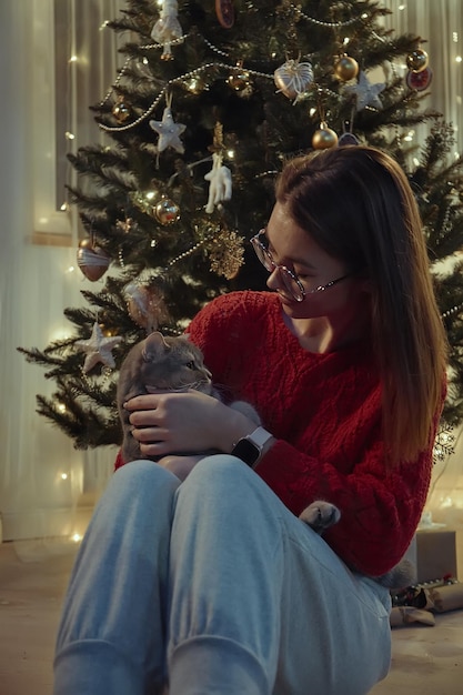 Jovem junto com um gato sentado perto da árvore de Natal Natal com um gato de estimação