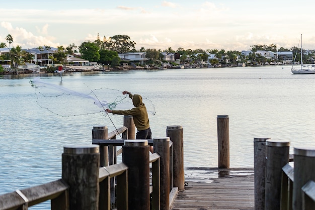 Foto jovem lançando uma rede de pesca para a água de uma doca.