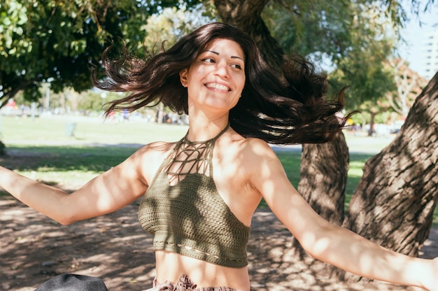 Jovem latina ao ar livre com os braços abertos dançando mexendo o cabelo e sorrindo
