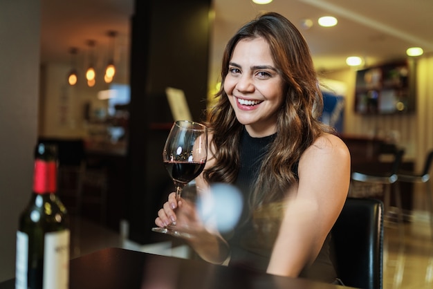 Jovem latina com uma taça de vinho tinto no bar