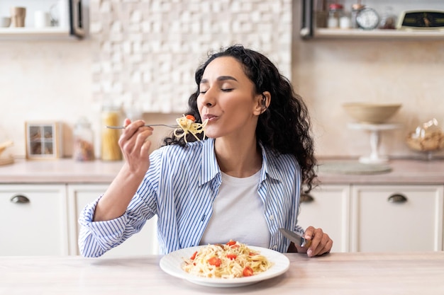 Foto jovem latina comendo deliciosas massas desfrutando de um saboroso almoço caseiro com os olhos fechados sentados em