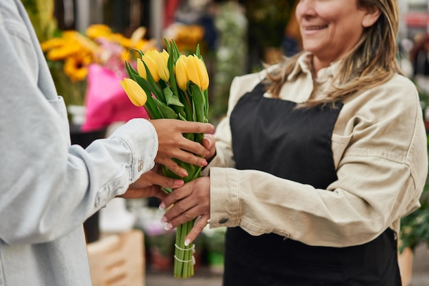 Jovem latina comprando flores vibrantes e plantas da barraca de um vendedor ambulante