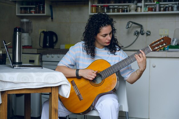 jovem latina concentrada em casa praticando nova música no violão