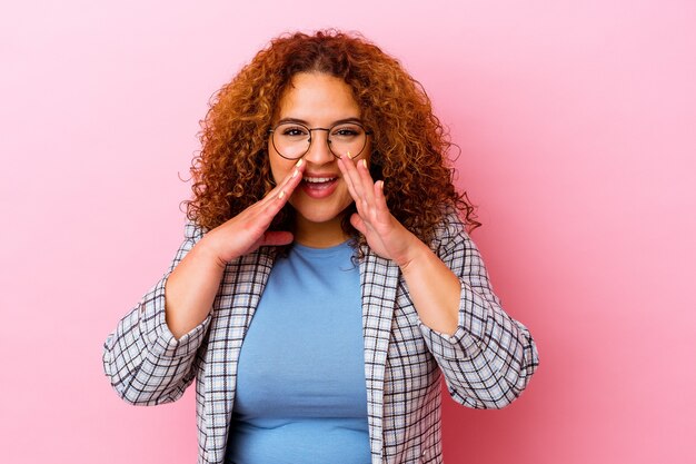 Foto jovem latina curvilínea isolada em um fundo rosa, dizendo uma fofoca, apontando para o lado relatando algo.