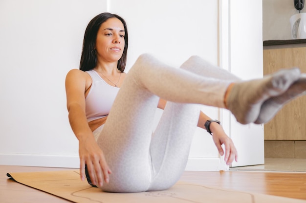 Jovem latina em roupas esportivas fazendo abdominais em uma esteira em sua sala de estar