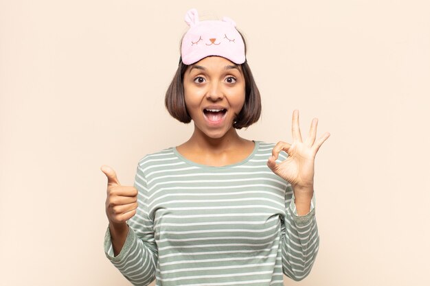 Jovem latina feliz, maravilhada, satisfeita e surpresa, mostrando gestos de ok e polegar para cima, sorrindo