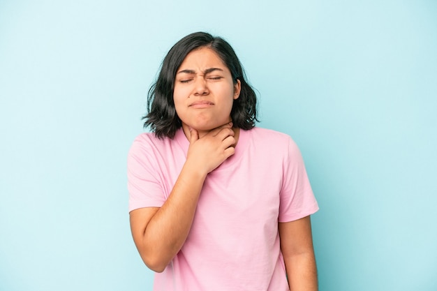 Jovem latina isolada em um fundo azul sofre de dor na garganta devido a um vírus ou infecção.
