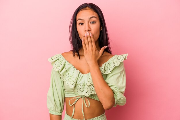 Jovem latina isolada em um fundo rosa chocada, cobrindo a boca com as mãos, ansiosa para descobrir algo novo.