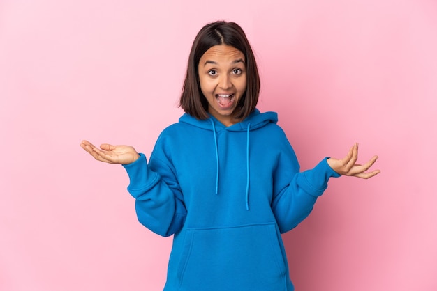 Jovem latina isolada em um fundo rosa com expressão facial chocada