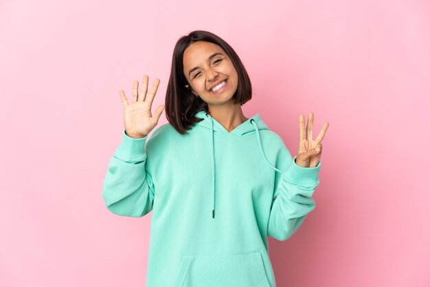 Jovem latina isolada em um fundo rosa contando oito com os dedos