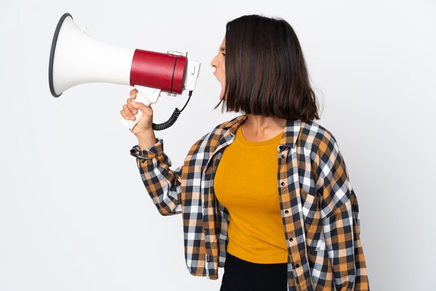 Jovem latina isolada na superfície branca gritando em um megafone para anunciar algo em posição lateral