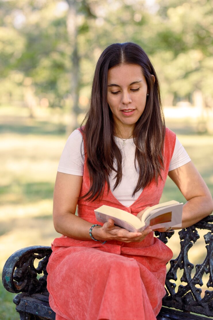 Jovem latina lendo um livro sentada em um banco de parque, estudando ao ar livre