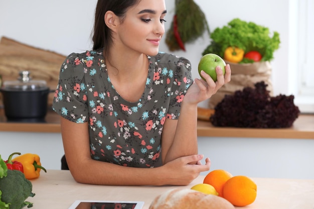 Jovem latina mordendo maçã verde Dona de casa encontrou uma nova receita para cozinhar alimentos na cozinha