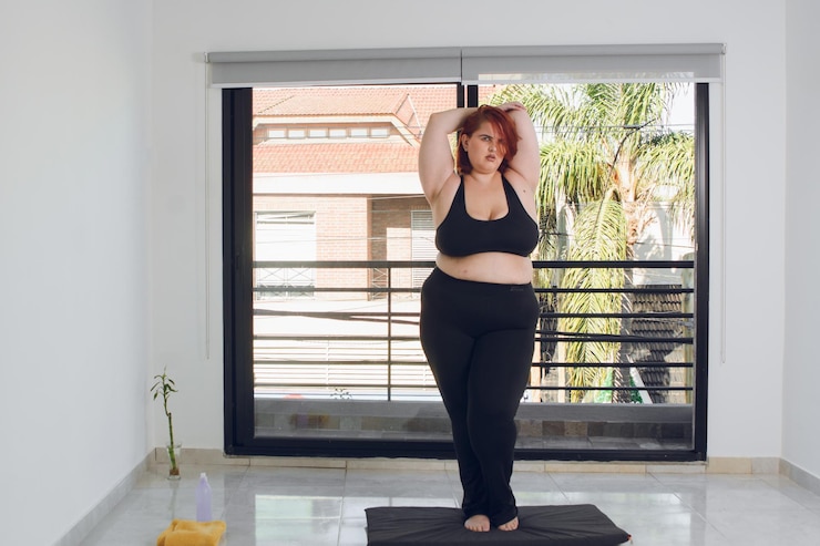 Foto jovem latina plus size se alongando dentro de casa antes de iniciar o treinamento físico