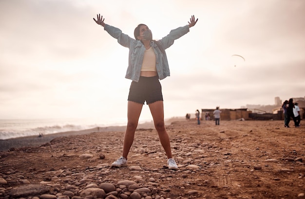 Jovem latina posa andando na areia durante um belo pôr do sol Jovem feliz com máscara