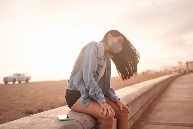 Foto jovem latina posa andando na areia durante um belo pôr do sol jovem feliz com máscara