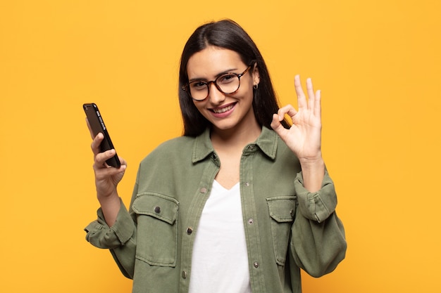 Jovem latina se sentindo feliz, relaxada e satisfeita, mostrando aprovação com gesto de ok, sorrindo