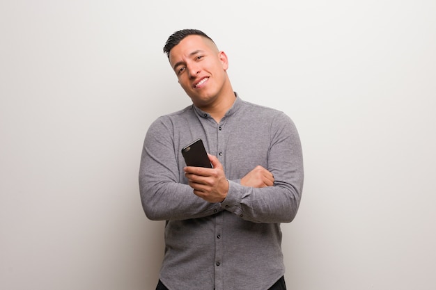 Jovem latina segurando um telefone sorrindo confiante e cruzando os braços, olhando para cima