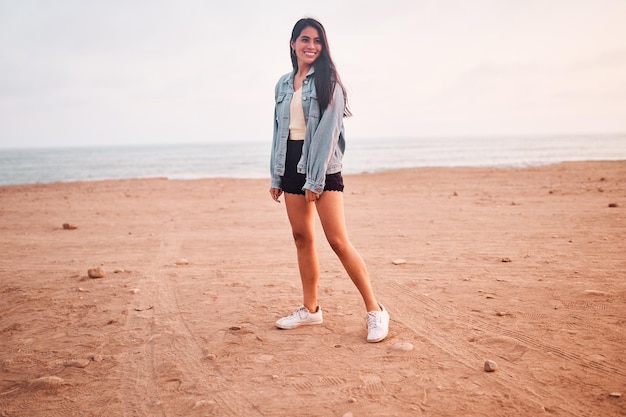 Jovem latina sorri durante um belo pôr do sol Jovem feliz com máscara na praia tomando