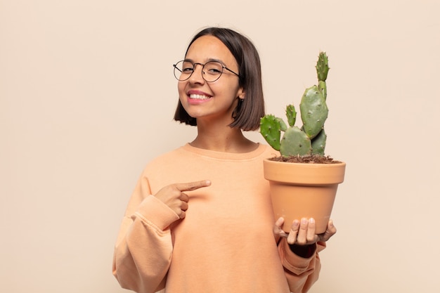 Jovem latina sorrindo alegremente, sentindo-se feliz e apontando para o lado e para cima, mostrando o objeto no espaço da cópia