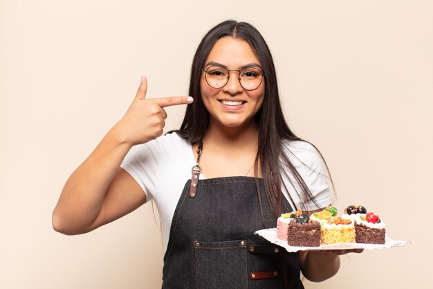 Jovem latina sorrindo com confiança apontando para o próprio sorriso largo, atitude positiva, relaxada e satisfeita