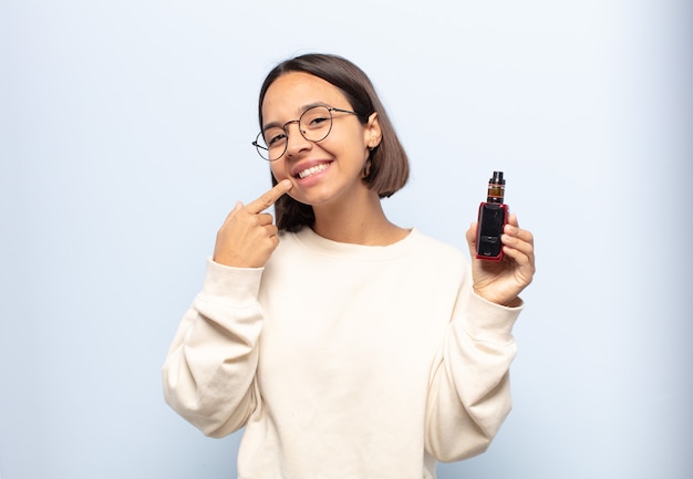 Jovem latina sorrindo com confiança apontando para o próprio sorriso largo, atitude positiva, relaxada e satisfeita