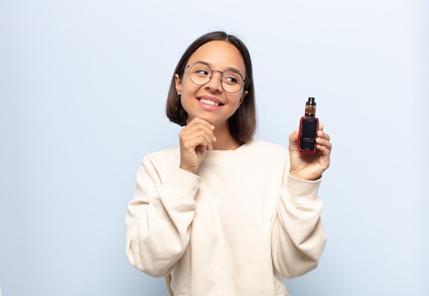 Jovem latina sorrindo com uma expressão feliz e confiante com a mão no queixo, pensando e olhando para o lado