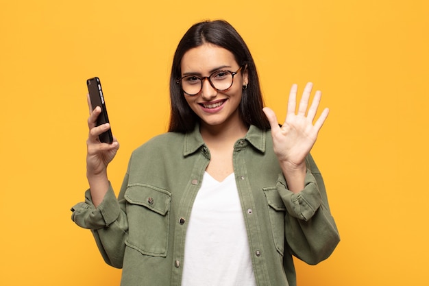 Jovem latina sorrindo e parecendo amigável, mostrando o número cinco ou quinto com a mão para a frente, em contagem regressiva