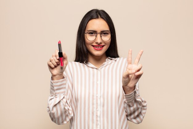 Jovem latina sorrindo e parecendo amigável, mostrando o número dois ou o segundo com a mão para a frente, em contagem regressiva