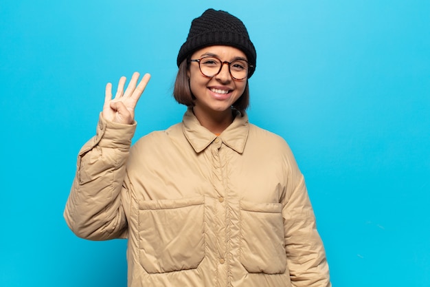 Jovem latina sorrindo e parecendo amigável, mostrando o número quatro ou o quarto com a mão para a frente, em contagem regressiva