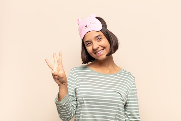 Jovem latina sorrindo e parecendo amigável, mostrando o número três ou o terceiro com a mão para a frente, em contagem regressiva