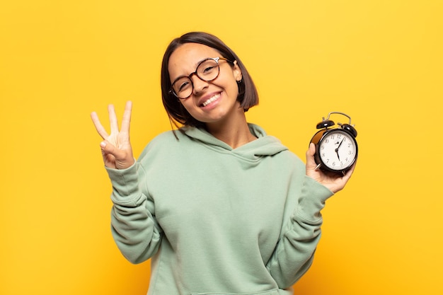 Jovem latina sorrindo e parecendo amigável, mostrando o número três ou o terceiro com a mão para a frente, em contagem regressiva