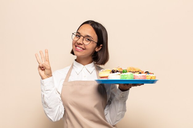 Jovem latina sorrindo e parecendo amigável, mostrando o número três ou terceiro com a mão para a frente, em contagem regressiva