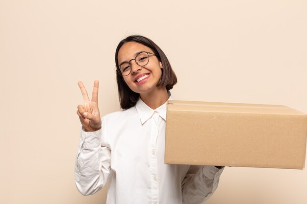 Jovem latina sorrindo e parecendo feliz, despreocupada e positiva, gesticulando vitória ou paz com uma mão