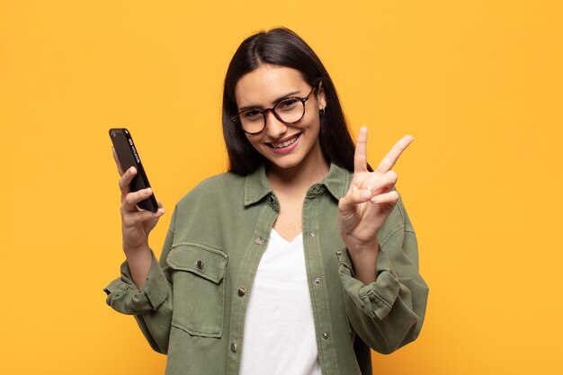 Jovem latina sorrindo e parecendo feliz, despreocupada e positiva, gesticulando vitória ou paz com uma mão