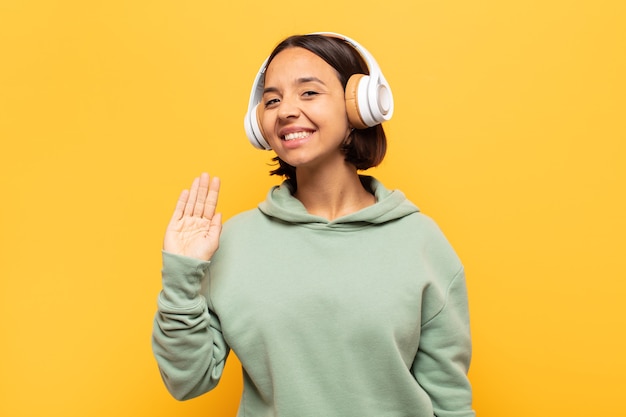 Jovem latina sorrindo feliz e alegre, acenando com a mão, dando as boas-vindas e cumprimentando você