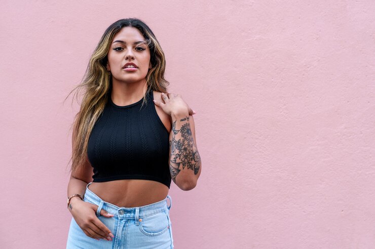 Foto jovem latina vestida casualmente mostra suas tatuagens contra um fundo rosa vibrante