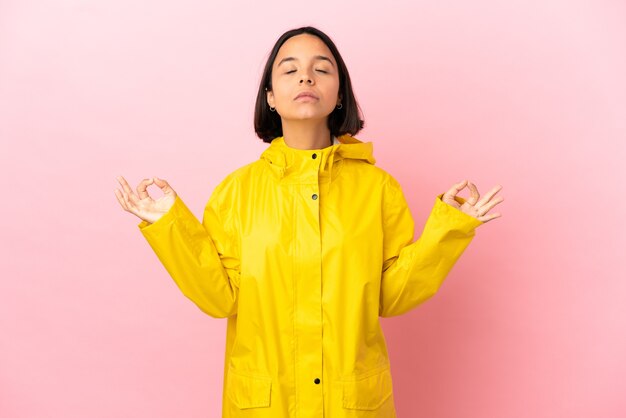 Jovem latina vestindo um casaco à prova de chuva sobre um fundo isolado em pose zen