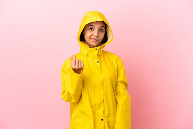 Foto jovem latina vestindo um casaco à prova de chuva sobre um fundo isolado fazendo gesto de dinheiro