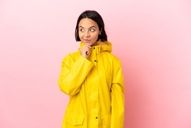 Foto jovem latina vestindo um casaco à prova de chuva sobre um fundo isolado pensando em uma ideia enquanto olha para cima