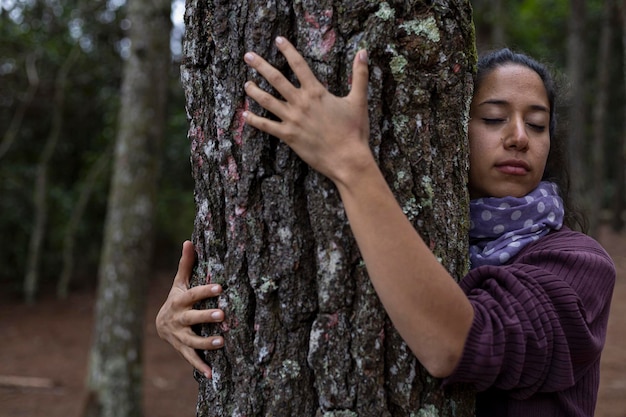 Foto jovem latino-americana 31 com olhos fechados abraça uma árvore em uma floresta de pinheiros conceito amor de aquecimento global pela percepção da vida da natureza