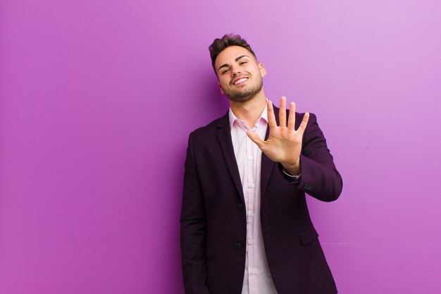 Jovem latino-americano, sorrindo e olhando amigável, mostrando o número cinco ou quinto com a mão para a frente, contando para baixo