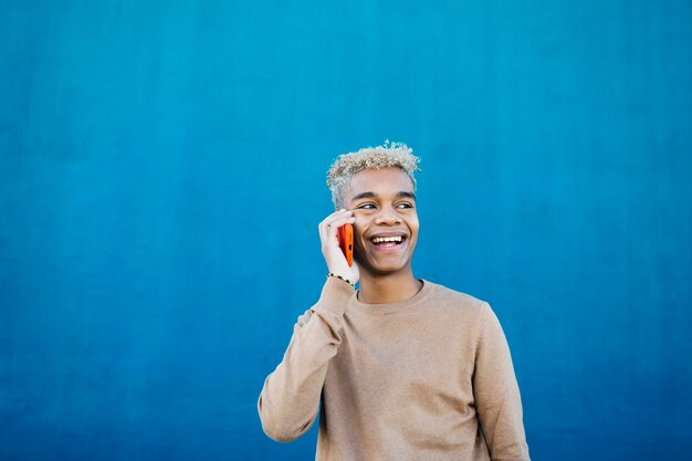 Foto jovem latino-americano usando um smartphone contra um fundo azul