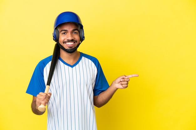 Jovem latino colombiano jogando beisebol isolado em um fundo amarelo apontando o dedo para o lado