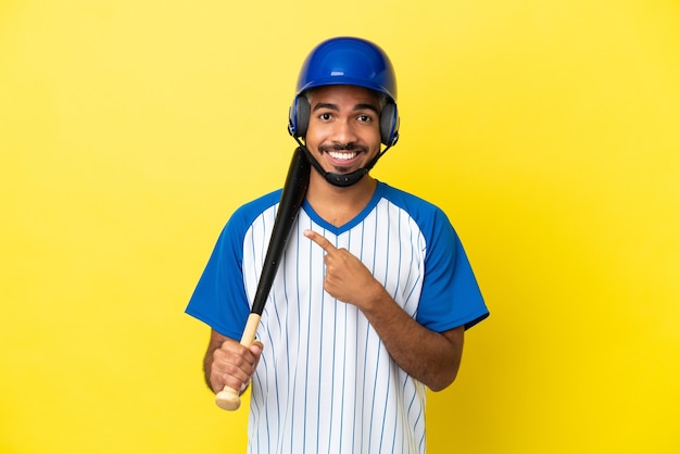 Jovem latino colombiano jogando beisebol isolado em um fundo amarelo apontando para o lado para apresentar um produto