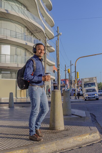 Jovem latino com fones de ouvido e roupas casuais atravessando a rua em uma cidade