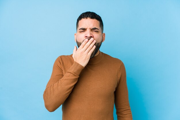 Jovem latino em um azul isolado bocejando mostrando um gesto cansado coning a boca com a mão.