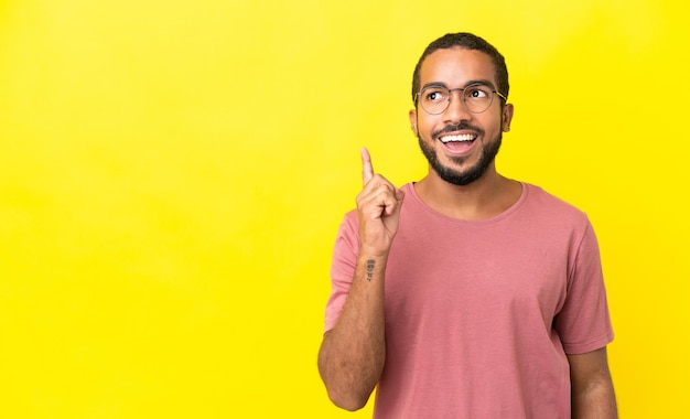 Jovem latino isolado em fundo amarelo pensando em uma ideia apontando o dedo para cima