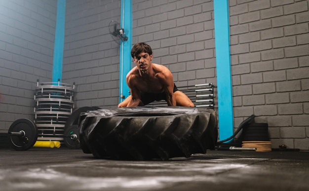 Jovem latino malhando com um pneu de trator em uma academia crossfit